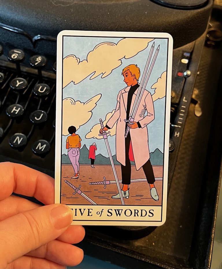 A picture of someone holding the Five of Swords tarot card. Image shows two people in background walking away and the victor in the foreground.